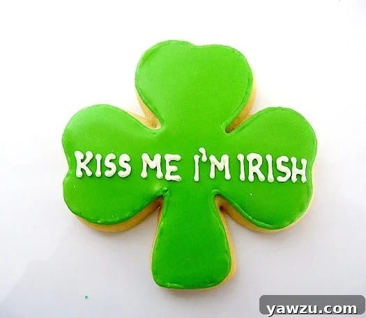 A festive shamrock sugar cookie, expertly covered in vivid green royal icing, featuring the playful phrase 'Kiss Me I'm Irish' intricately piped in crisp white lettering, a perfect St. Patrick's Day treat.