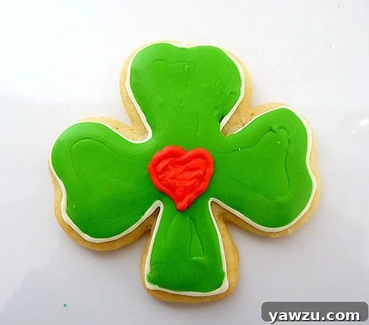 A beautifully decorated shamrock sugar cookie with rich green royal icing, featuring a charming bright red heart meticulously placed in its center, a unique and loving twist for St. Patrick's Day treats.