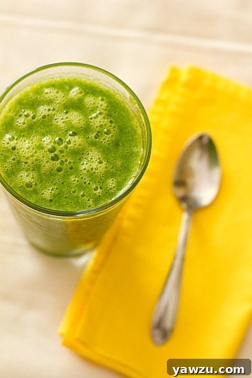 A vibrant green smoothie in a tall glass, garnished with a slice of lime, sits on a rustic wooden surface next to a fresh lime.