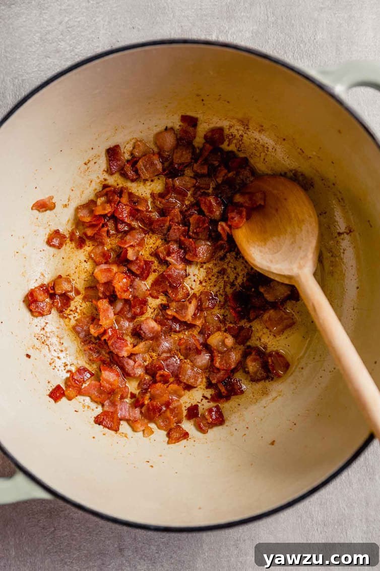 Close-up shot of thick-cut bacon strips sizzling and crisping in a white enameled Dutch oven over medium-low heat, rendering out their delicious fat.