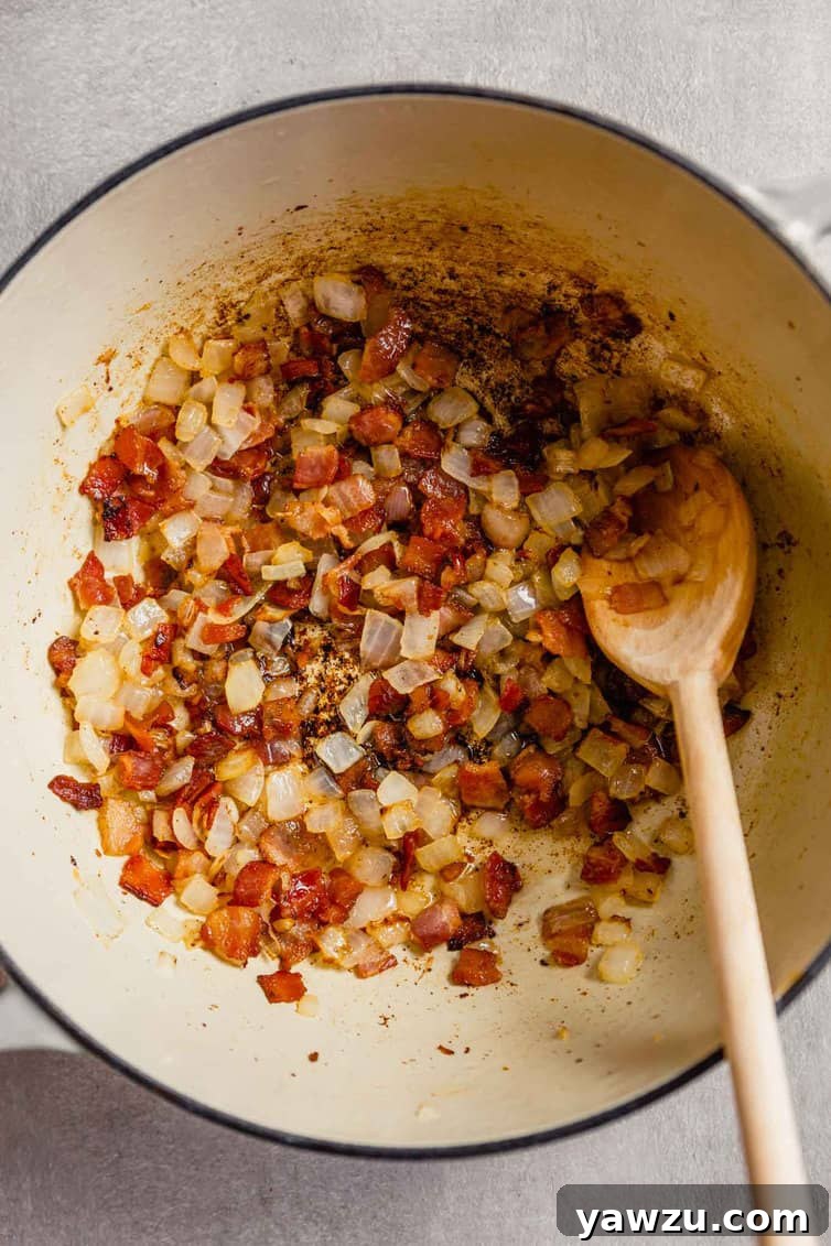 A white Dutch oven on the stovetop, with chopped thick-cut bacon and diced Spanish onions sizzling and sautéing together, creating an aromatic base for the chowder.