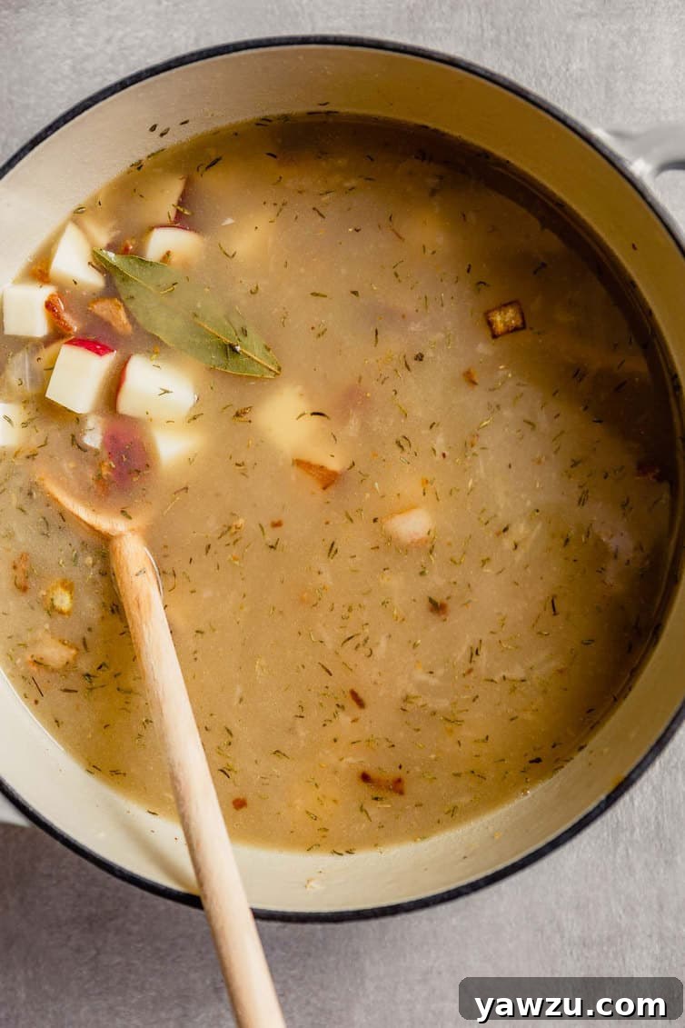 New England clam chowder simmering in a white Dutch oven, after the liquid base and diced red potatoes have been added, showing the potatoes softening in the flavorful broth.