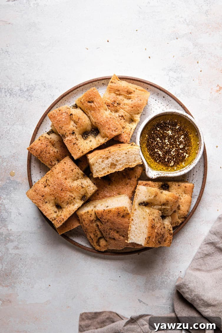 A top down photo of a small plate with a brown rim filled with a pile of sliced focaccia and a small herb oil bowl to the right.
