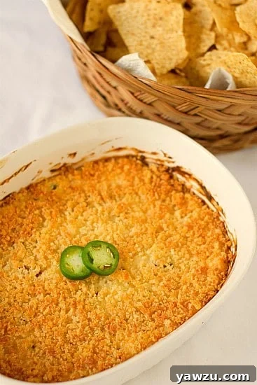 A bowl of creamy Jalapeno Popper Dip, topped with crunchy breadcrumbs and fresh jalapeño slices, served with crackers.