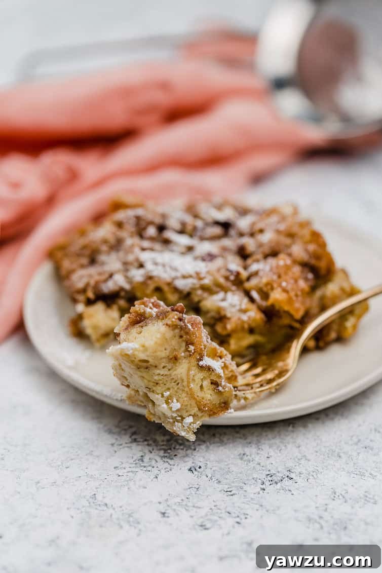 A piece of baked French toast with praline on a fork, with another piece on a plate in the background.