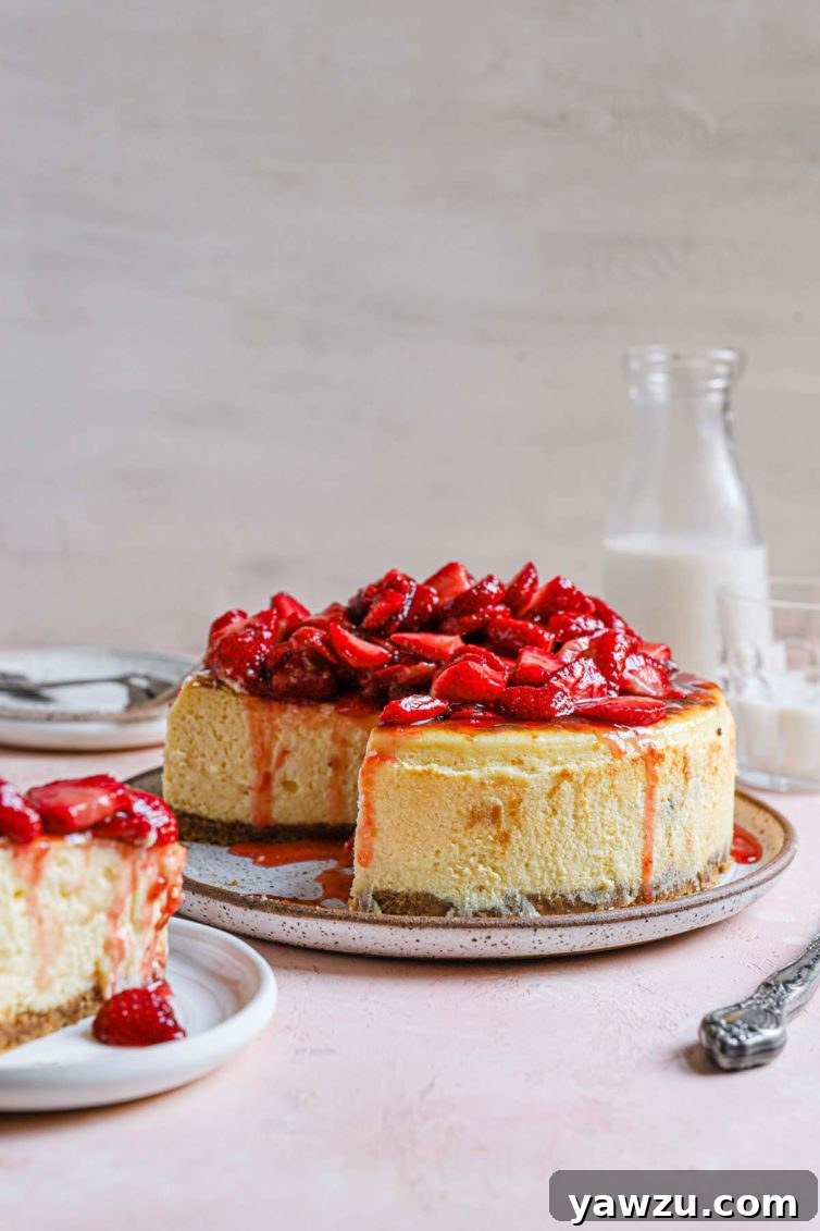 New York cheesecake topped with fresh strawberry sauce on a serving plate with a slice cut out.