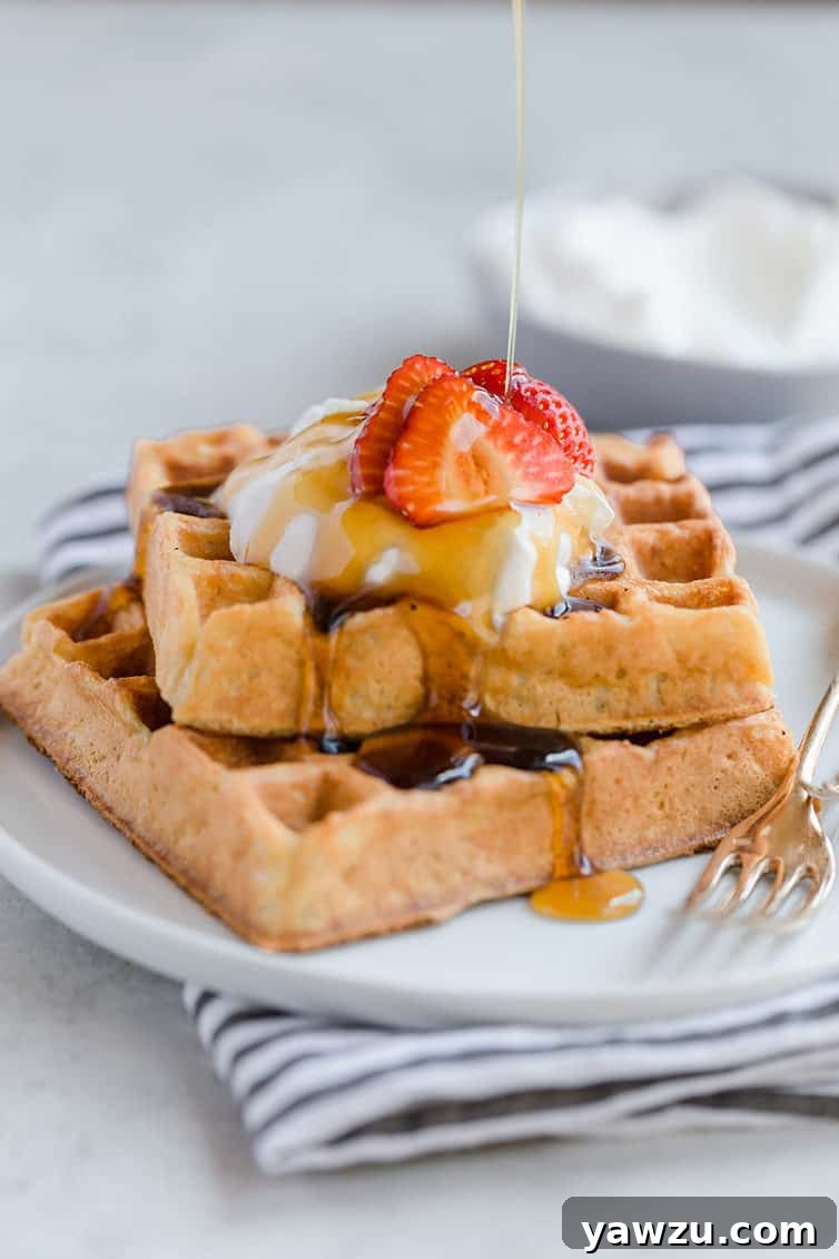 Two square waffles stacked with whipped cream and strawberries on top.