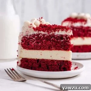 From the front a slice of red velvet cheesecake with layers of cake and cheesecake topped with cream cheese frosting and cake crumbs.