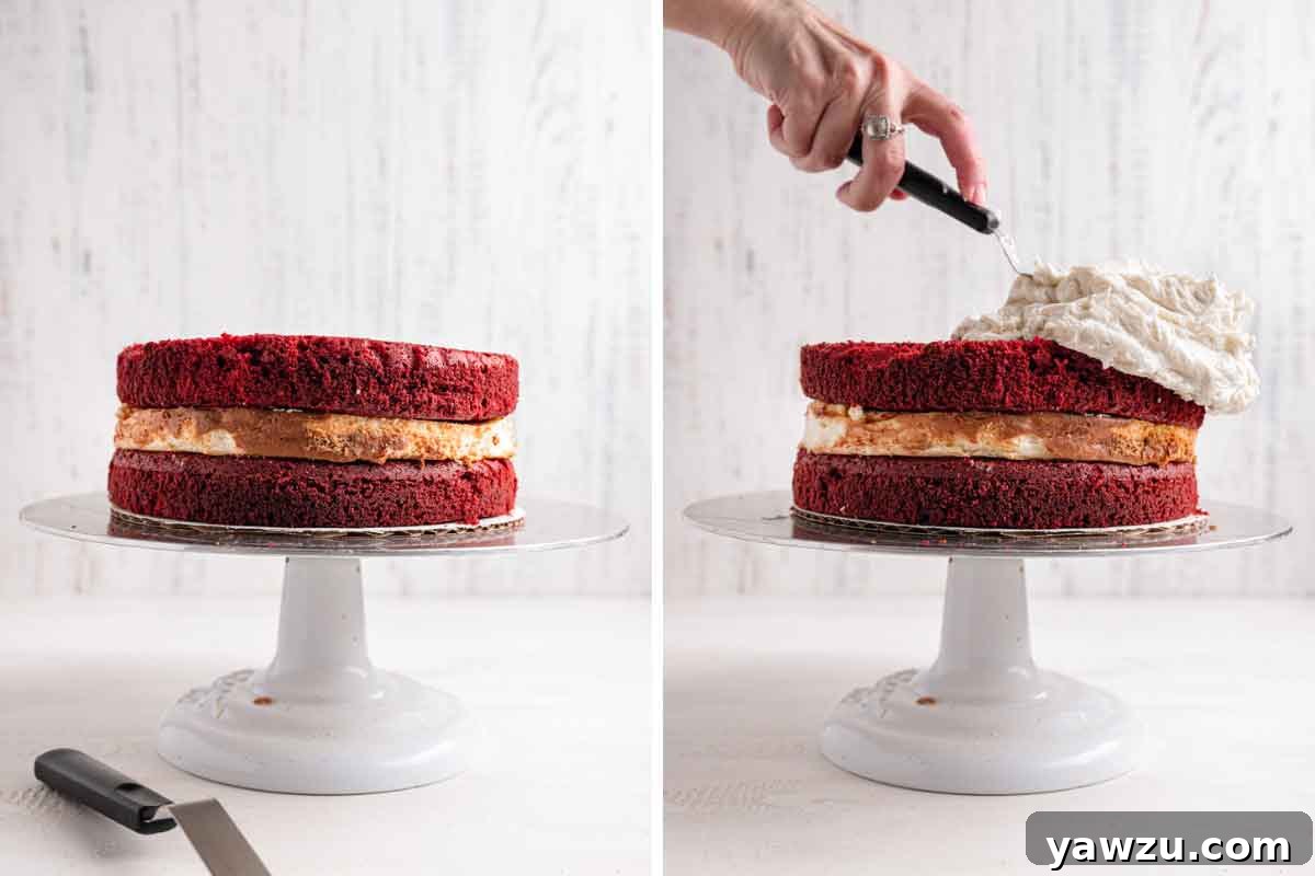 Red velvet cheesecake assembled on a cake stand, with cream cheese frosting being spread on top.