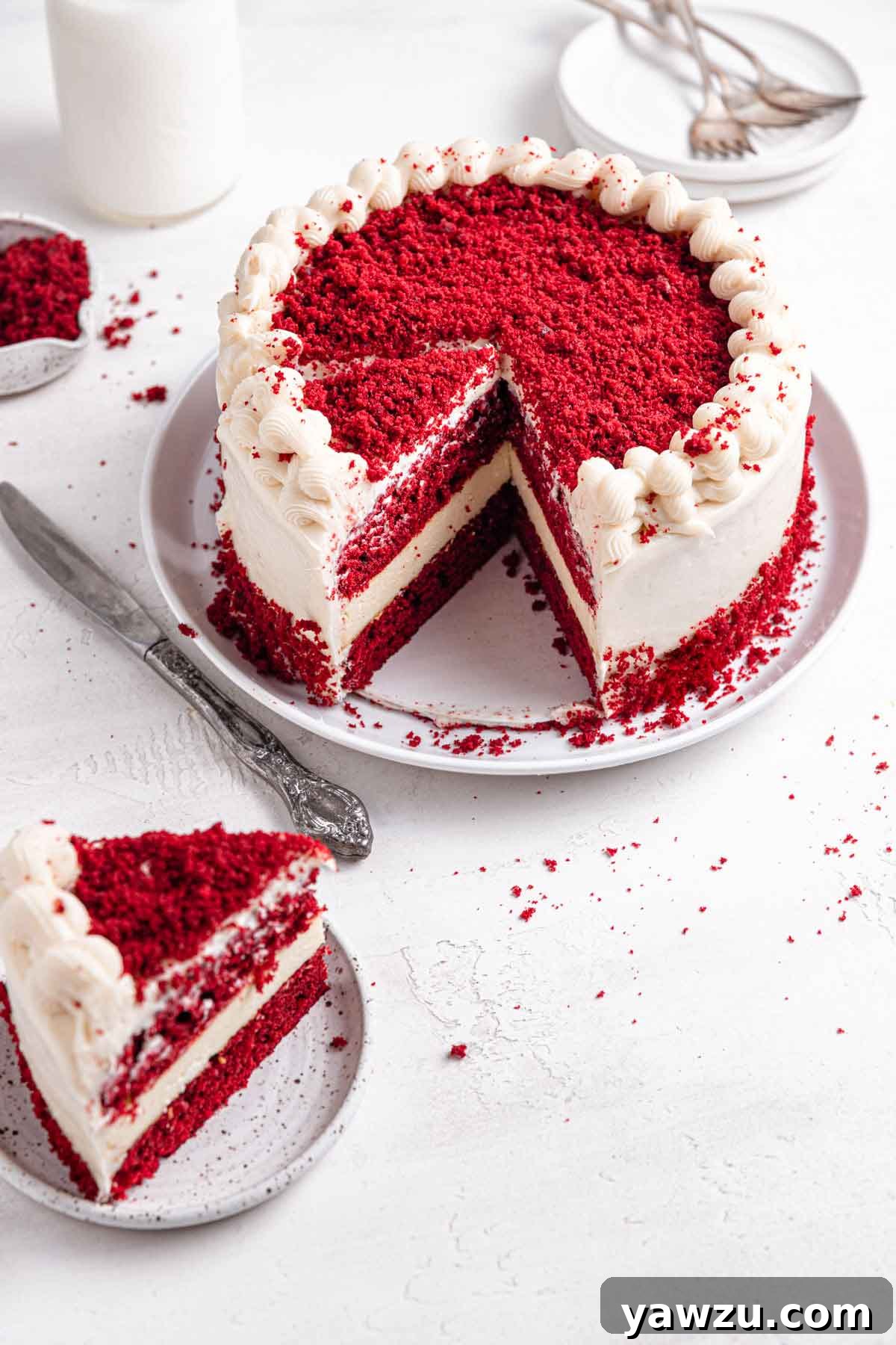 Assembled and decorated red velvet cheesecake on a serving platter with a single slice on a plate to the side.