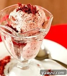 Scoops of red velvet ice cream in a glass bowl, garnished with a single cake crumb.