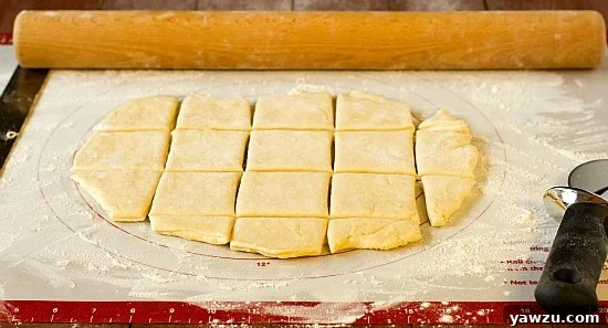 Beignet dough being expertly cut into squares on a floured surface, ready for frying.