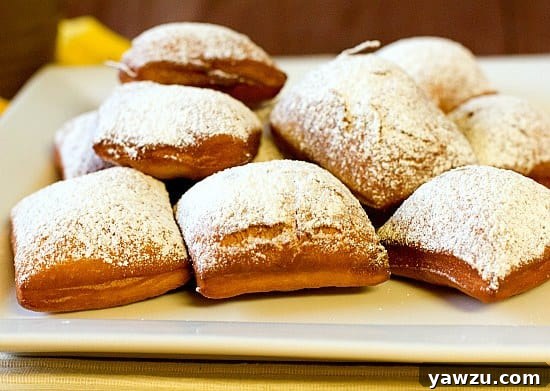A close-up of a stack of freshly made New Orleans Beignets, generously covered in powdered sugar, ready to be eaten.
