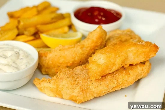 Golden brown beer battered cod fillets served with lemon wedges and a side of crispy french fries on a white plate, symbolizing a classic comfort food meal.