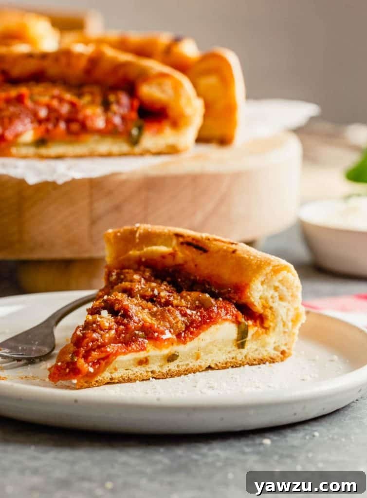 A perfectly baked slice of Chicago-style deep-dish pizza placed on a white plate, showcasing its thick crust, abundant cheese, and chunky sauce. The rest of the deep-dish pizza is visible in the background, ready for more slices.