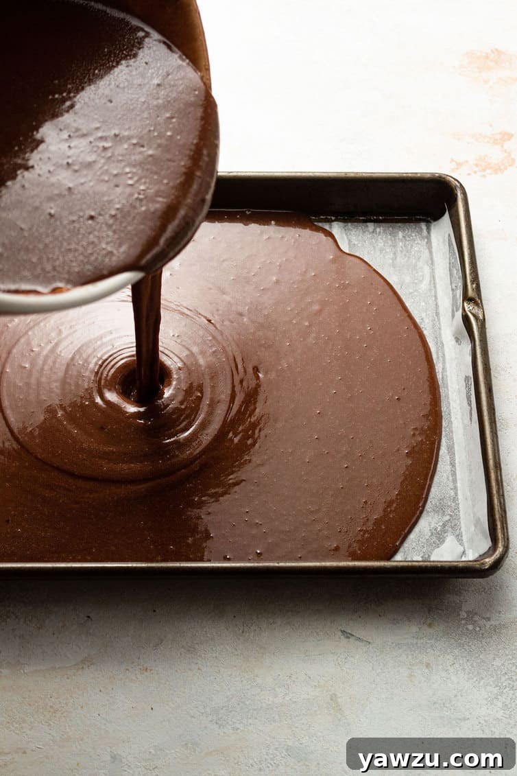 Pouring rich chocolate cake batter into a prepared sheet pan, ready for baking.