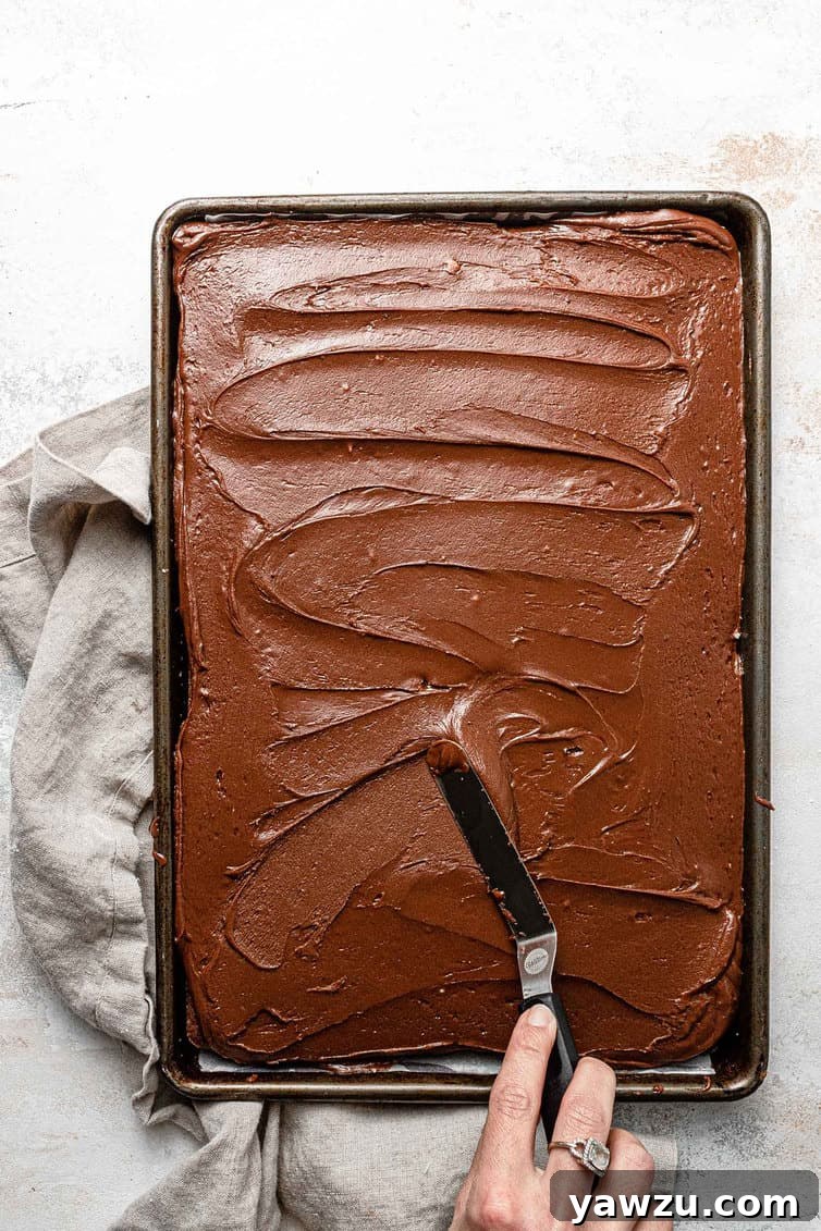 Expertly spreading warm chocolate frosting over a freshly baked Texas sheet cake with an offset spatula.