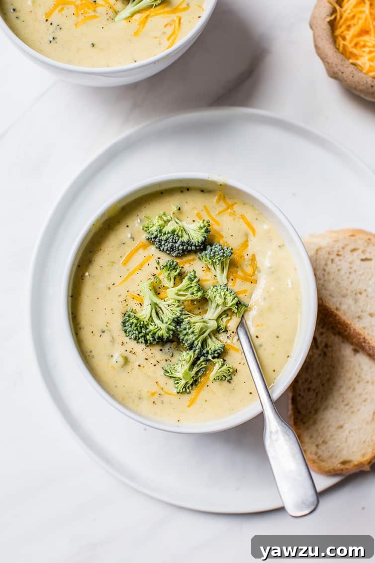 A steaming bowl of creamy broccoli cheese soup, garnished with a sprinkle of cheddar and fresh parsley, served with crusty bread on the side.