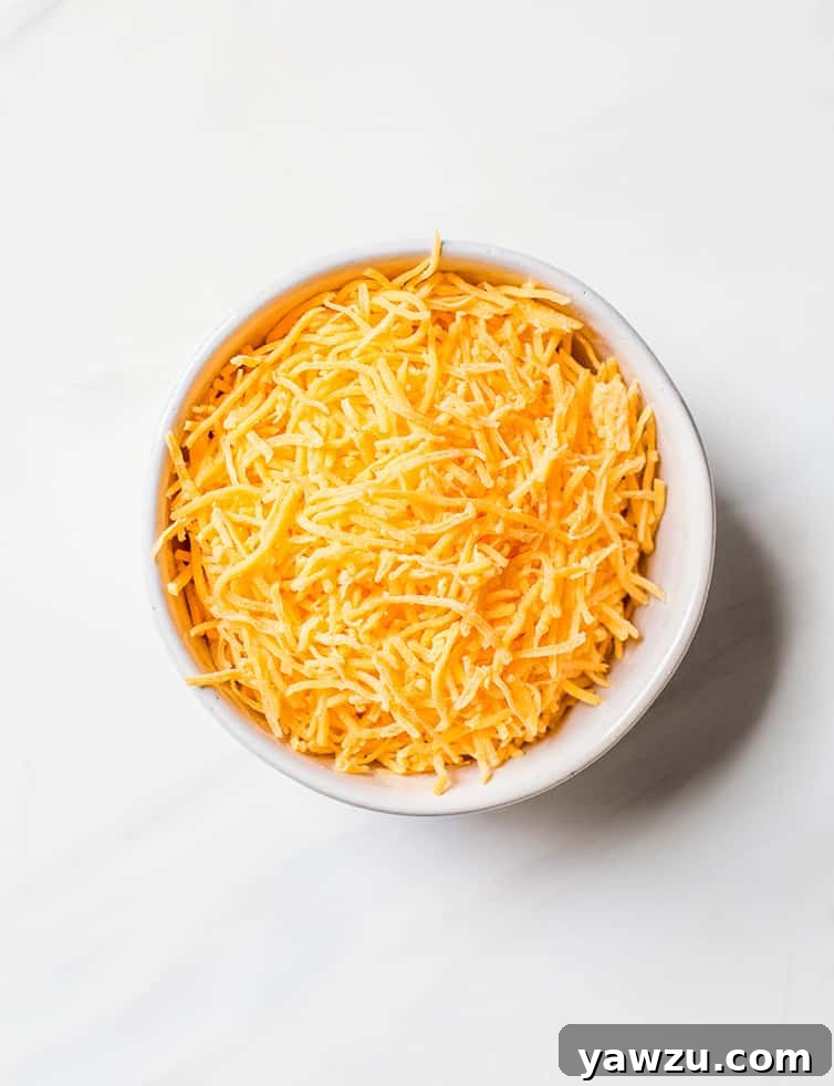 A clear prep bowl filled with a generous mound of freshly shredded cheddar cheese, a key ingredient for a rich and flavorful soup.
