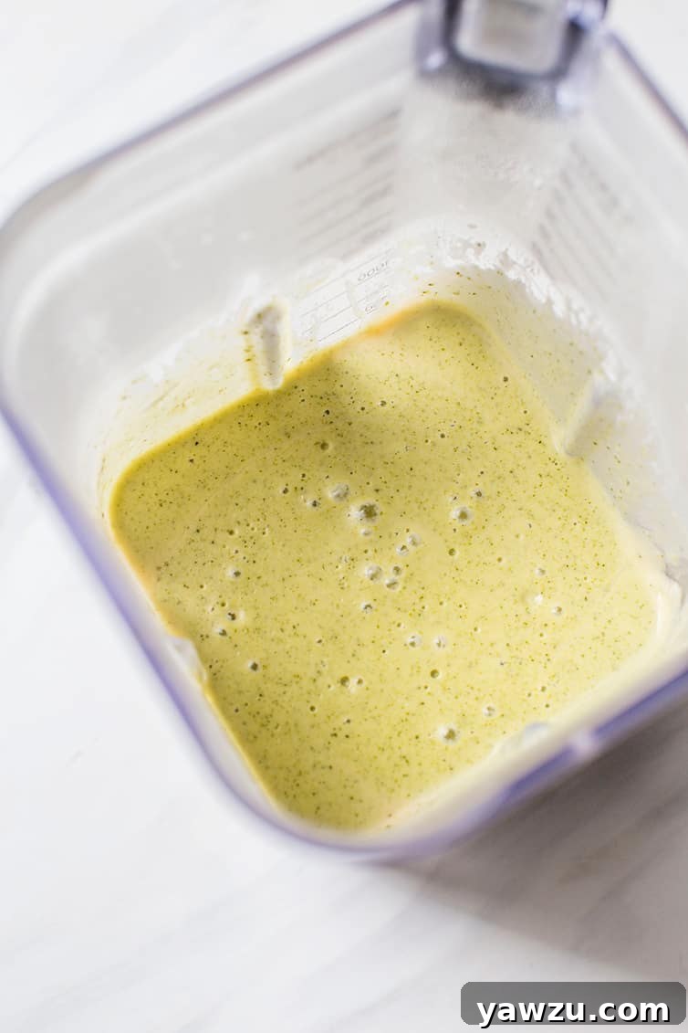 A vibrant green broccoli cheese soup being pureed in a blender, showing the transformation to a smooth, creamy texture.