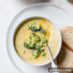 A bowl of broccoli cheese soup with bread on the side.