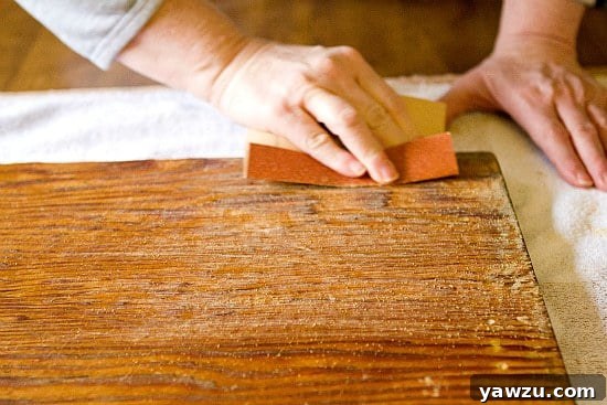 Close-up of a wooden dough board being meticulously sanded with coarse 80-grit sandpaper, revealing smoother wood underneath