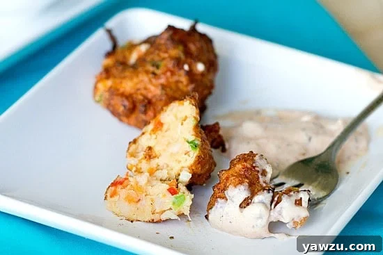 A plate of golden-brown conch fritters with a side of dipping sauce, garnished with fresh herbs.