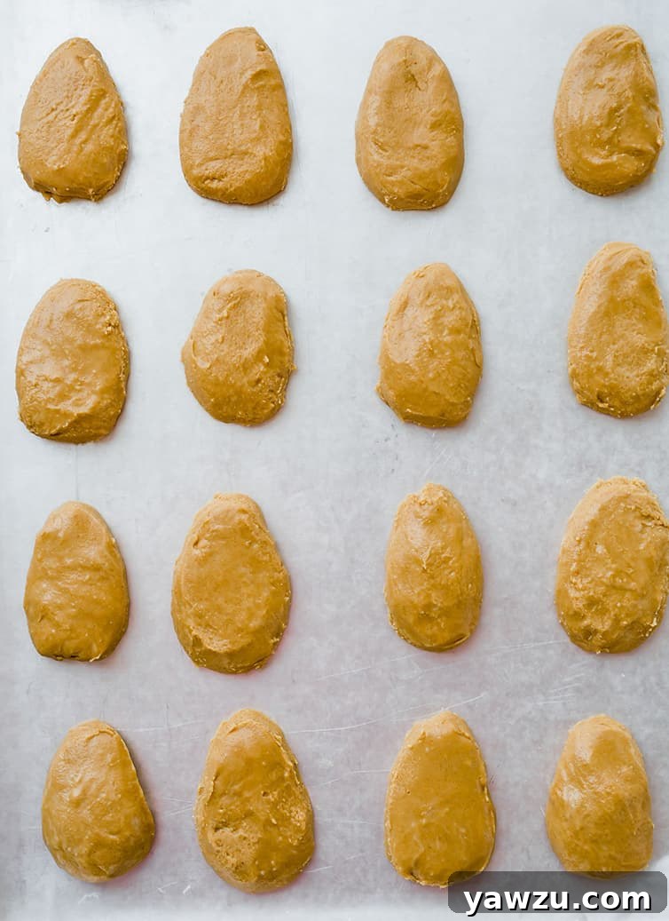 Perfectly shaped peanut butter eggs, awaiting their chocolate coating, neatly arranged on a baking pan lined with parchment paper.