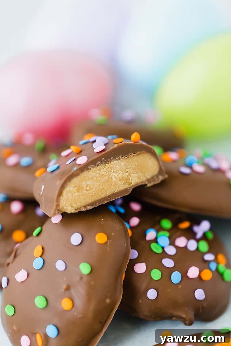 A close-up of a perfectly halved peanut butter egg, resting atop a small stack of whole peanut butter eggs, highlighting its smooth texture.