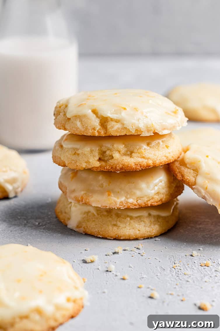 A stack of perfectly glazed orange cookies with a refreshing glass of milk in the background, ready to be enjoyed.