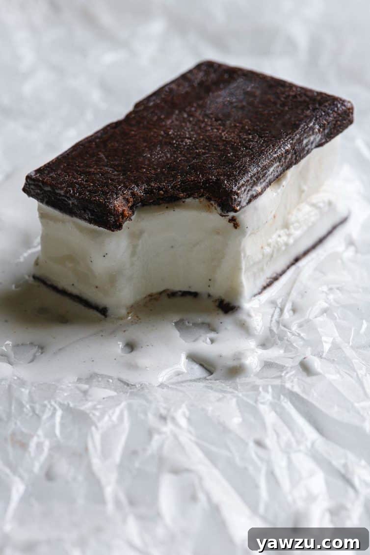 A homemade ice cream sandwich with a bite take out and a little melted on the parchment paper.