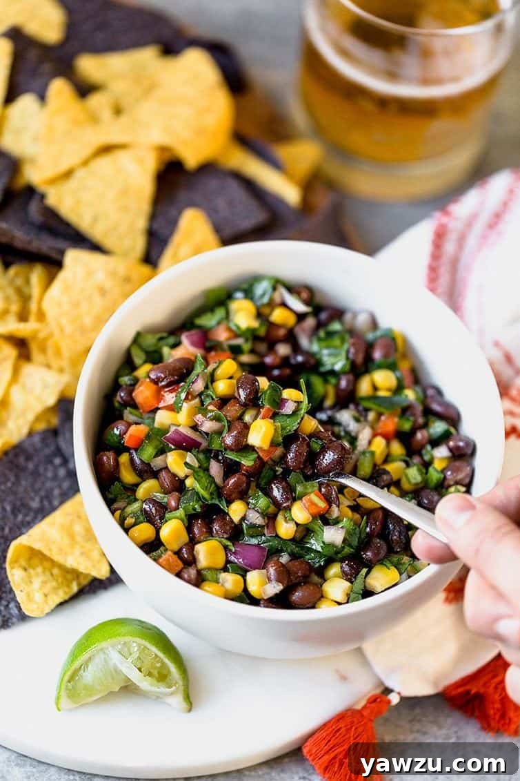 A close-up shot of a hand scooping a generous spoonful of homemade black bean salsa from a rustic bowl.