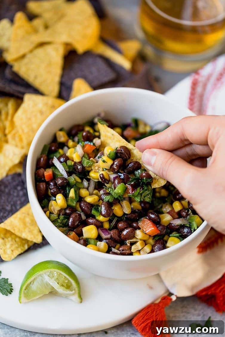 A hand expertly dipping a crunchy tortilla chip into a rich, chunky bowl of black bean salsa.