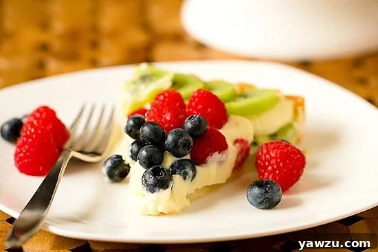 Beautifully arranged kiwi, raspberry, and blueberry tart with creamy filling
