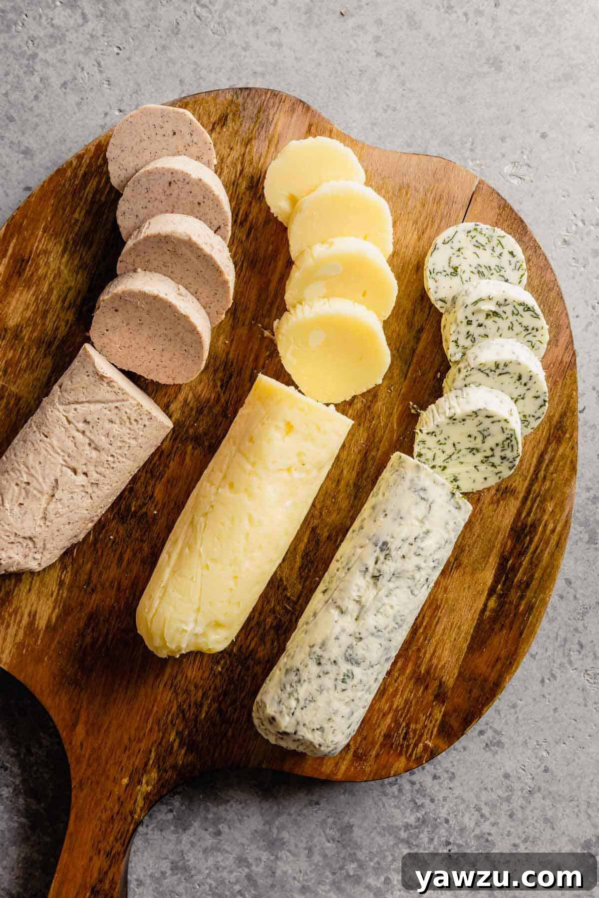 A wooden cutting board showcasing three distinct types of homemade compound butter on a chic grey countertop.