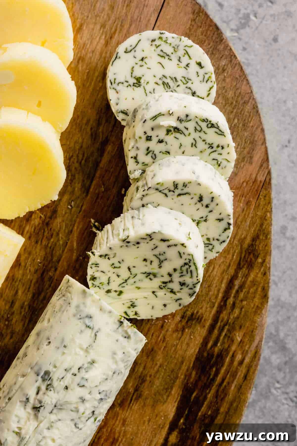 A top-down view of a beautifully sliced log of garlic and herb compound butter on a wooden board.