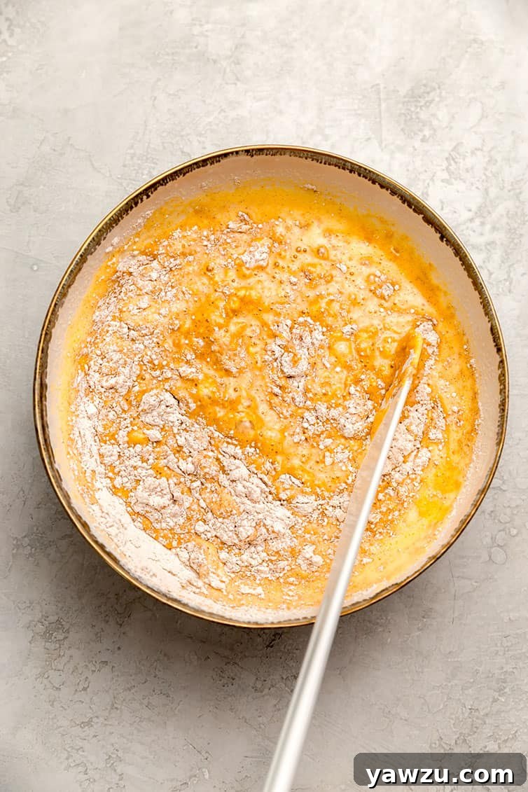A mixing bowl filled with vibrant orange pumpkin roll batter, ready for pouring into the pan.