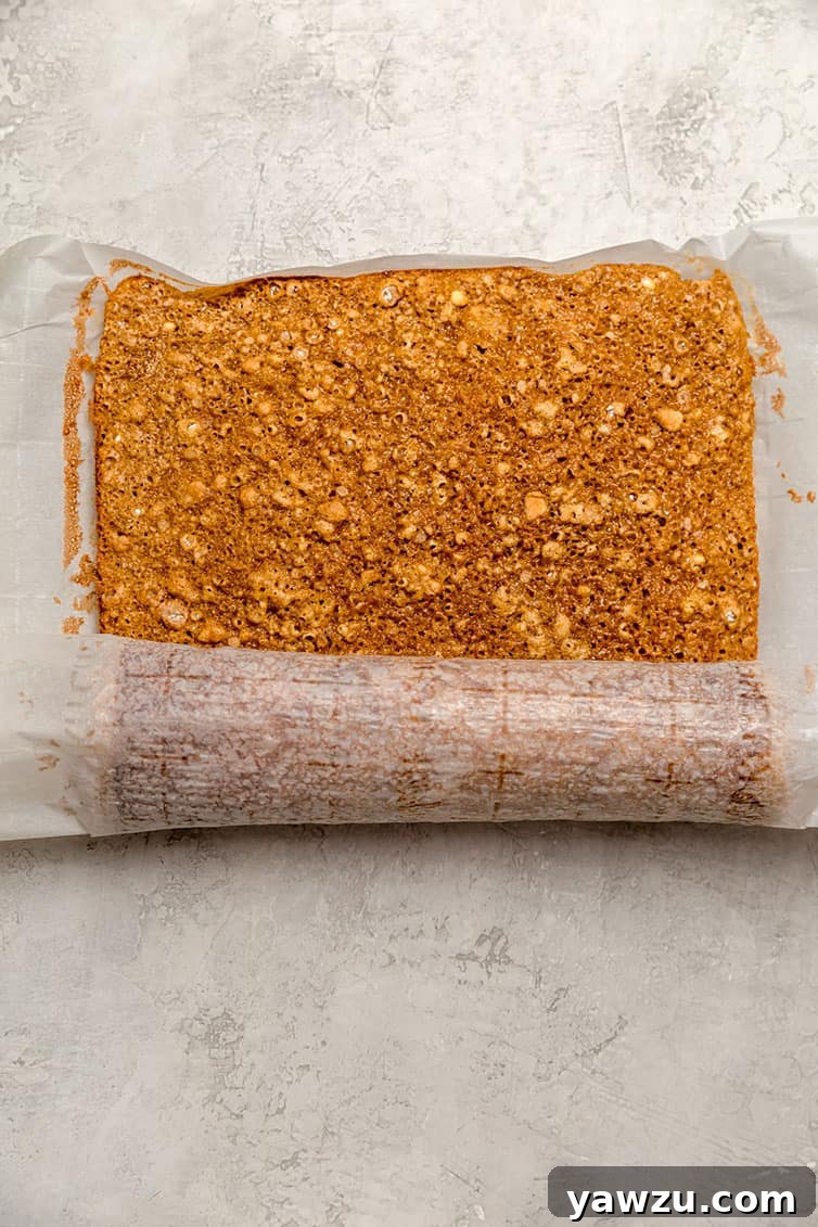 A baked pumpkin roll cake being gently rolled up in parchment paper after baking, demonstrating the new technique.