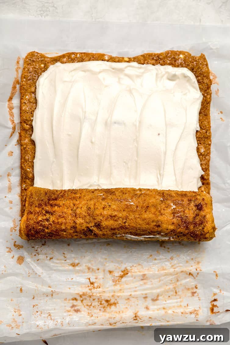 A pumpkin roll being gently re-rolled after the cream cheese frosting has been applied, ready for chilling.