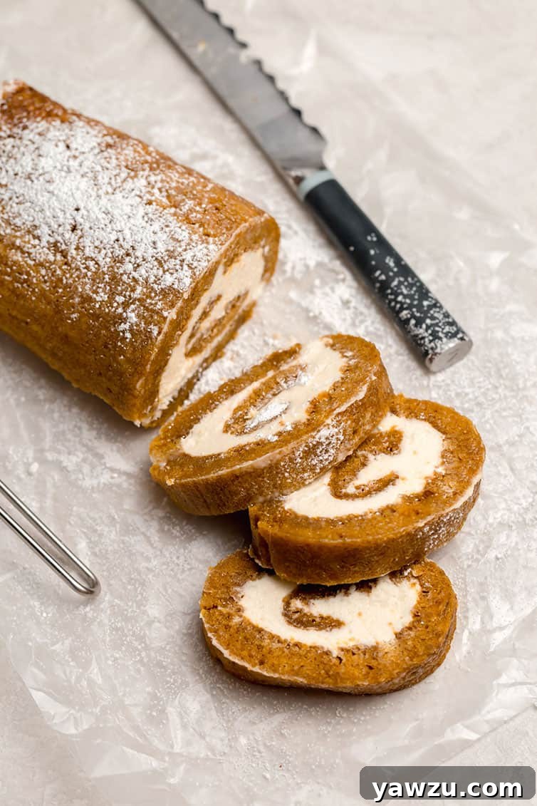 A pumpkin roll, partially sliced, showcasing its perfect spiral, on a piece of parchment paper.