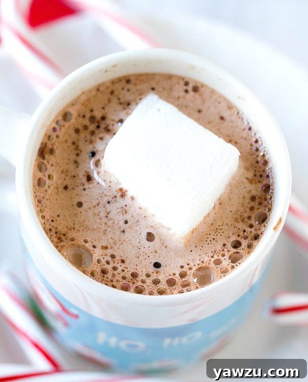 Freshly cut homemade peppermint marshmallows, some plain white, others half-dipped in dark chocolate and rolled in crushed candy canes, on a cutting board.