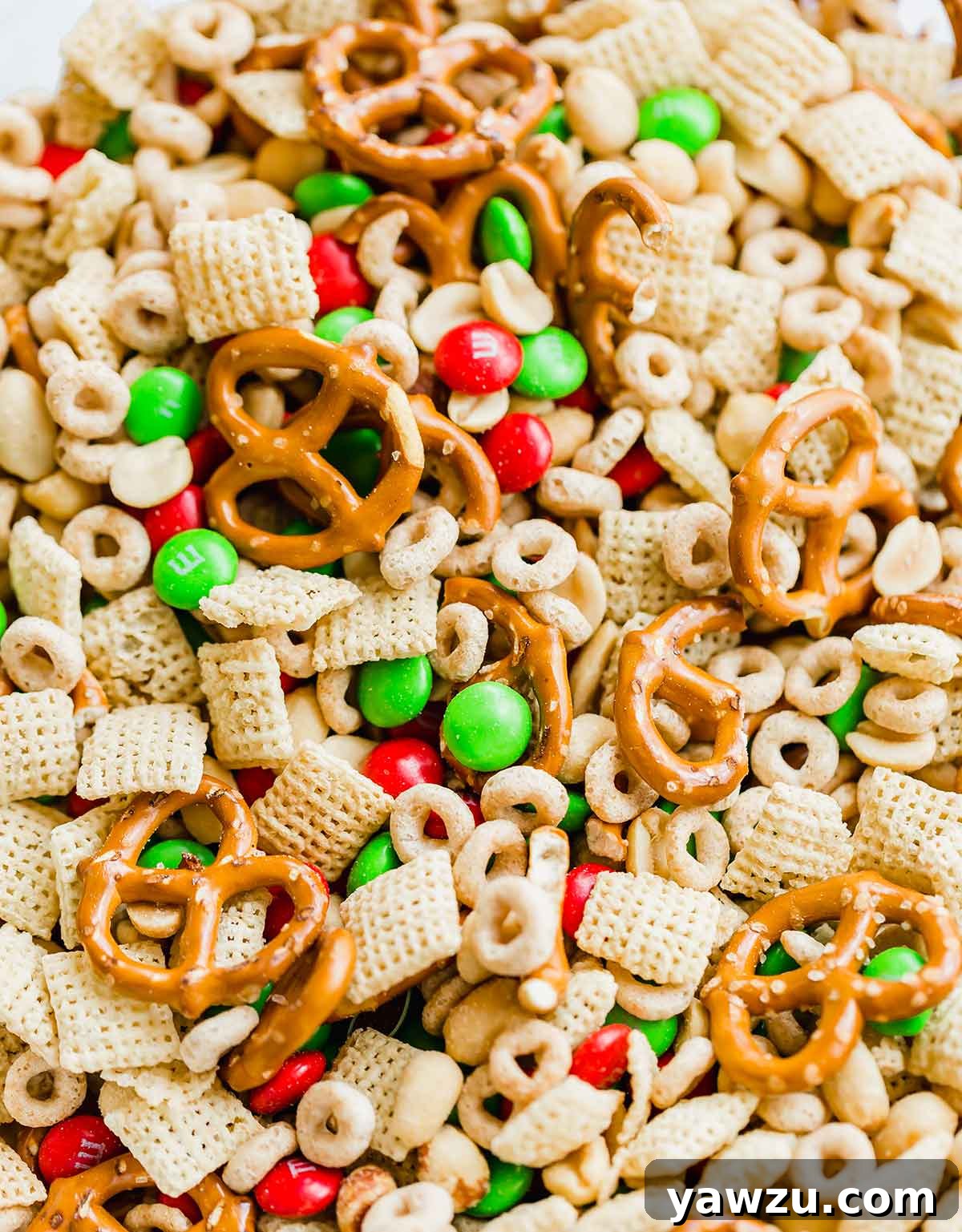 Closeup photo of ingredients for reindeer chow in a bowl - Rice Chex, Cheerios, peanuts, pretzels, and M&Ms, ready to be mixed.