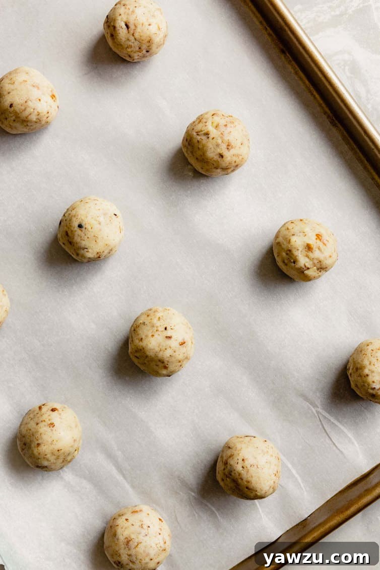 Snowball cookie dough rolled into small balls and arranged on a parchment-lined baking sheet.