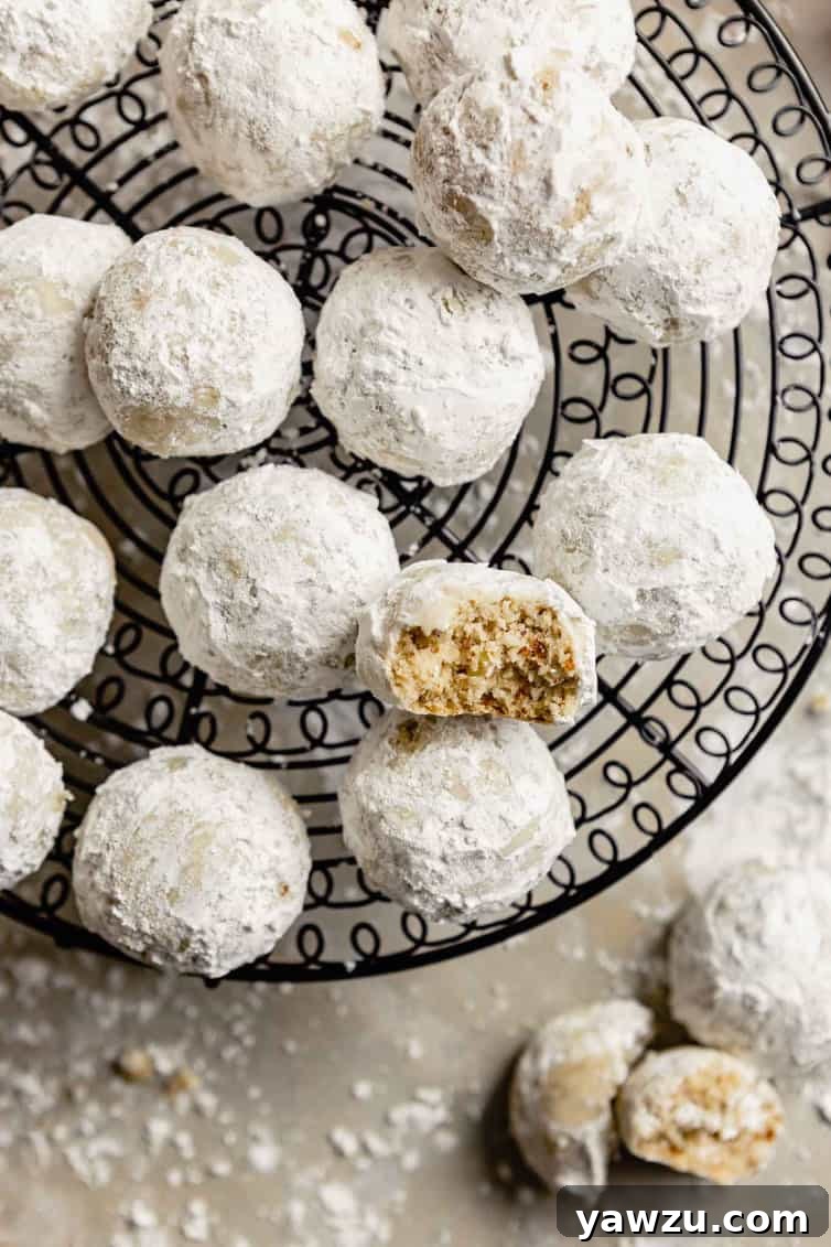 Close-up of baked Snowball Cookies on a wire cooling rack, one half-eaten.