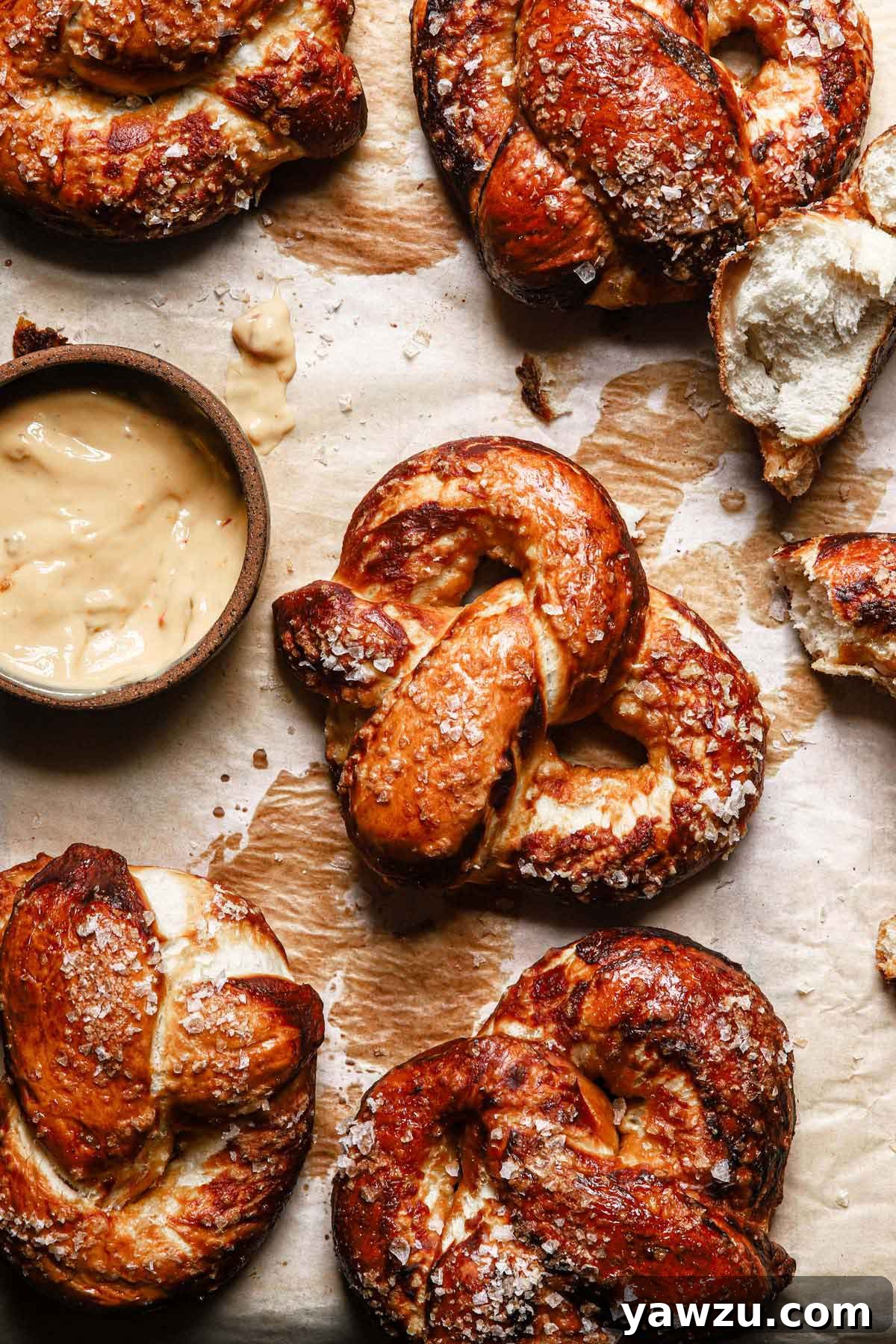Overhead photo of golden-brown homemade soft pretzels on parchment paper, ready to be served, with a bowl of spicy cheese dipping sauce nearby.