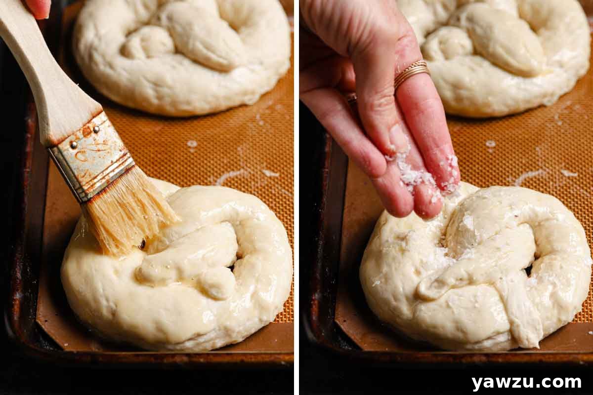 A close-up shot of soft pretzels being brushed with an egg wash and sprinkled with coarse salt, preparing them for baking.