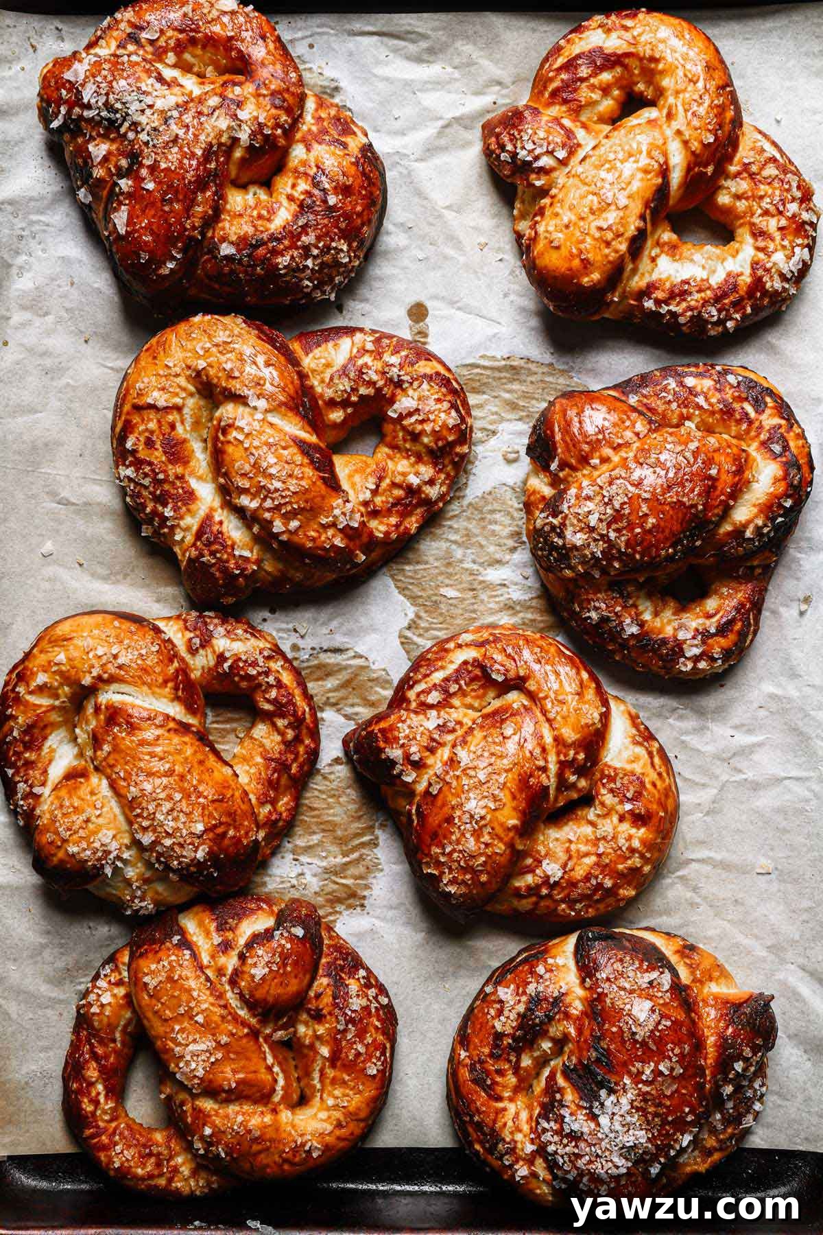 A batch of freshly baked, golden-brown soft pretzels cooling on parchment paper, glistening with salt and ready to be enjoyed.