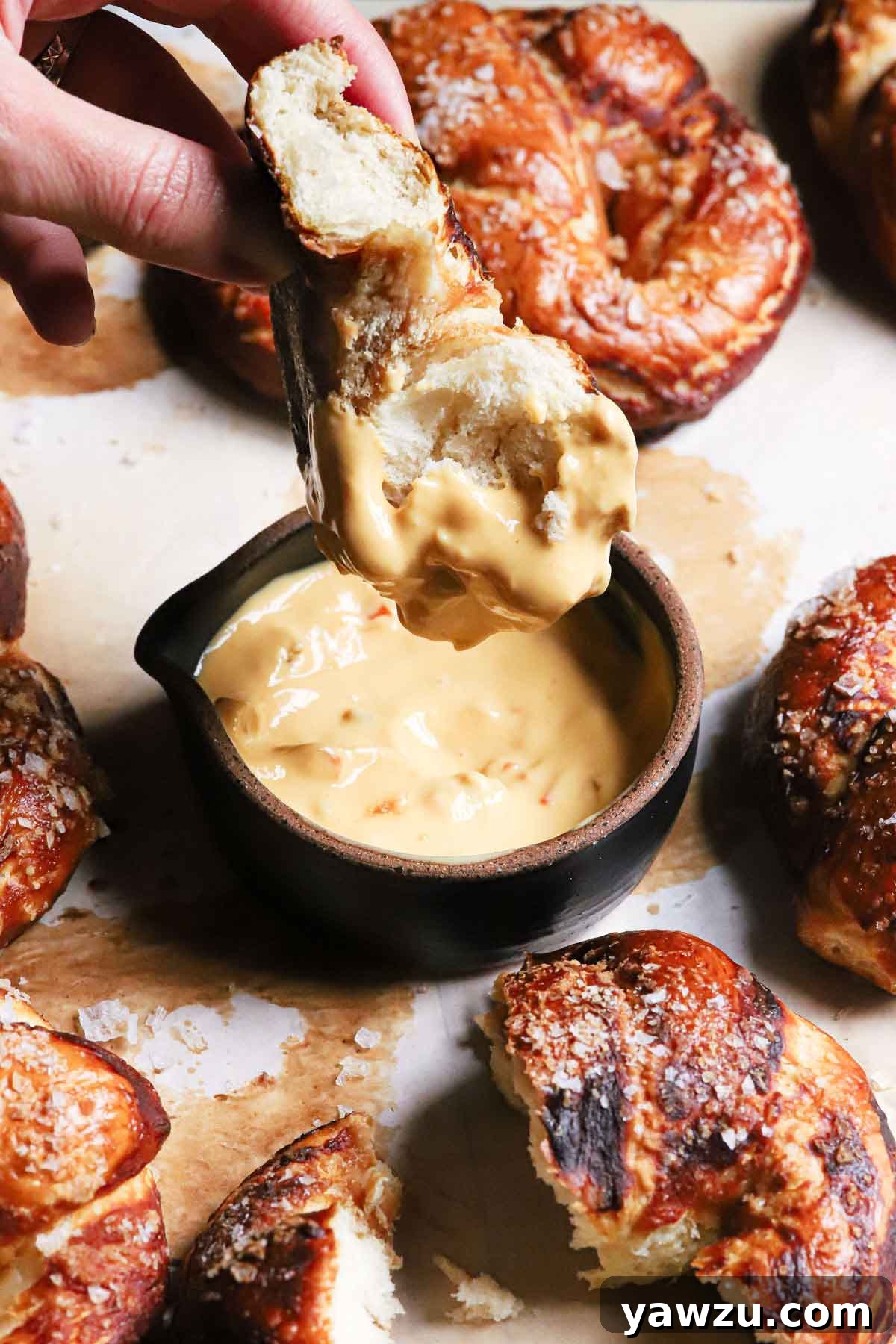A freshly baked soft pretzel bite being dipped into a small, tempting bowl of spicy cheese sauce, ready for enjoyment.