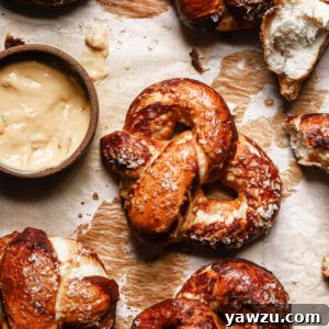 homemade soft pretzels on a baking tray garniched with coarse salt and with a beer cheese dipping sauce on the side
