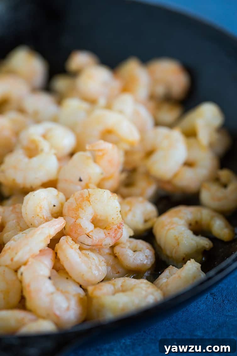 A skillet of freshly sauteed shrimp, seasoned with Cajun spices, ready to be incorporated into the creamy macaroni and cheese.